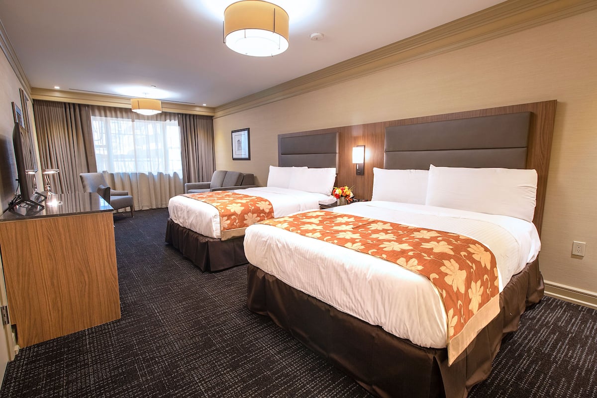 Une chambre d’hôtel avec deux lits, un bureau et une grande fenêtre avec des rideaux.