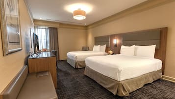 A hotel room with two beds, a desk, and a bench.