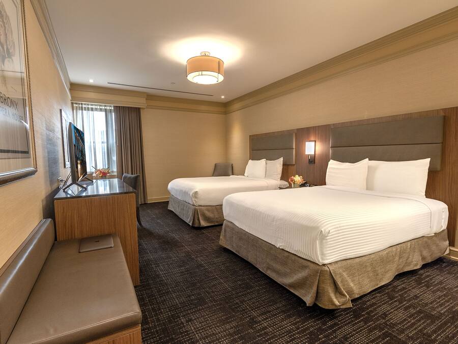 A hotel room with two beds, a desk, and a bench.