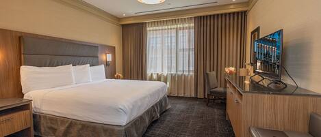 Habitación de hotel con una cama grande, un escritorio con una computadora portátil, un televisor y una ventana con cortinas.