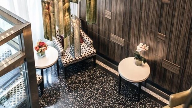 A modern interior with a dark wood panel wall, a glass partition, and two small round tables with floral centerpieces. - Opera House Hotel (Bronx)