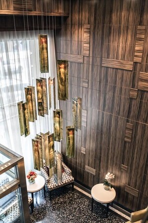 A modern interior with a dark wood panel wall, a glass partition, and two small round tables with floral centerpieces. - Opera House Hotel (Bronx)