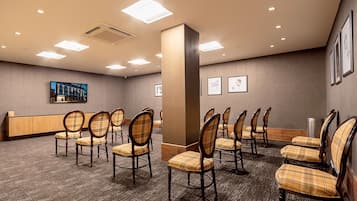 Uma sala de conferências com fileiras de cadeiras de madeira com estofamento xadrez, uma mesa de recepção e obras de arte emolduradas nas paredes.