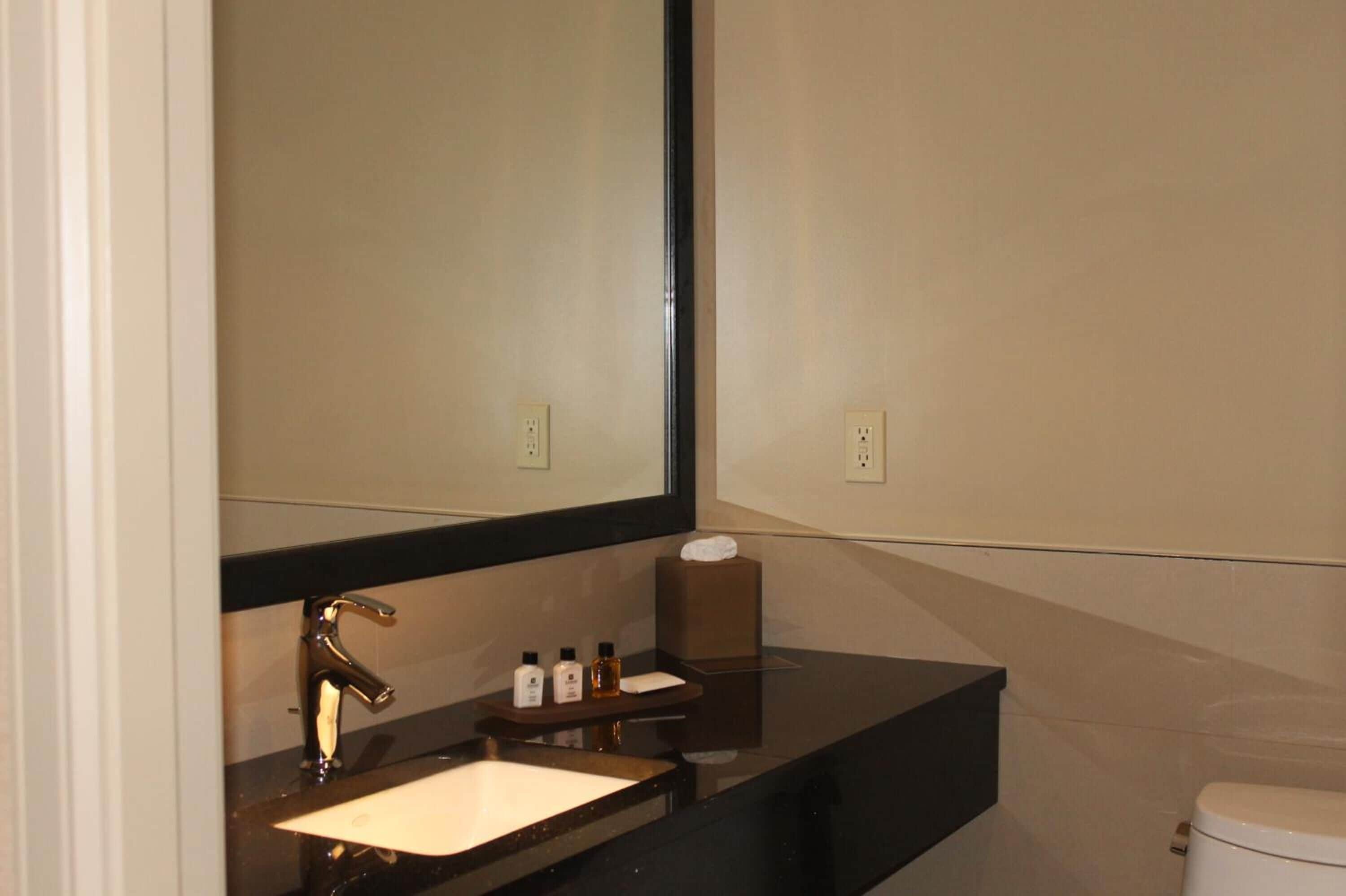Uma casa de banho moderna com bancada preta, lavatório branco, espelho grande e sanita.
