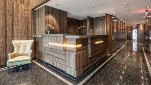 A modern reception area with a wooden reception desk, a plush armchair, and a polished marble floor. - Opera House Hotel (Bronx)