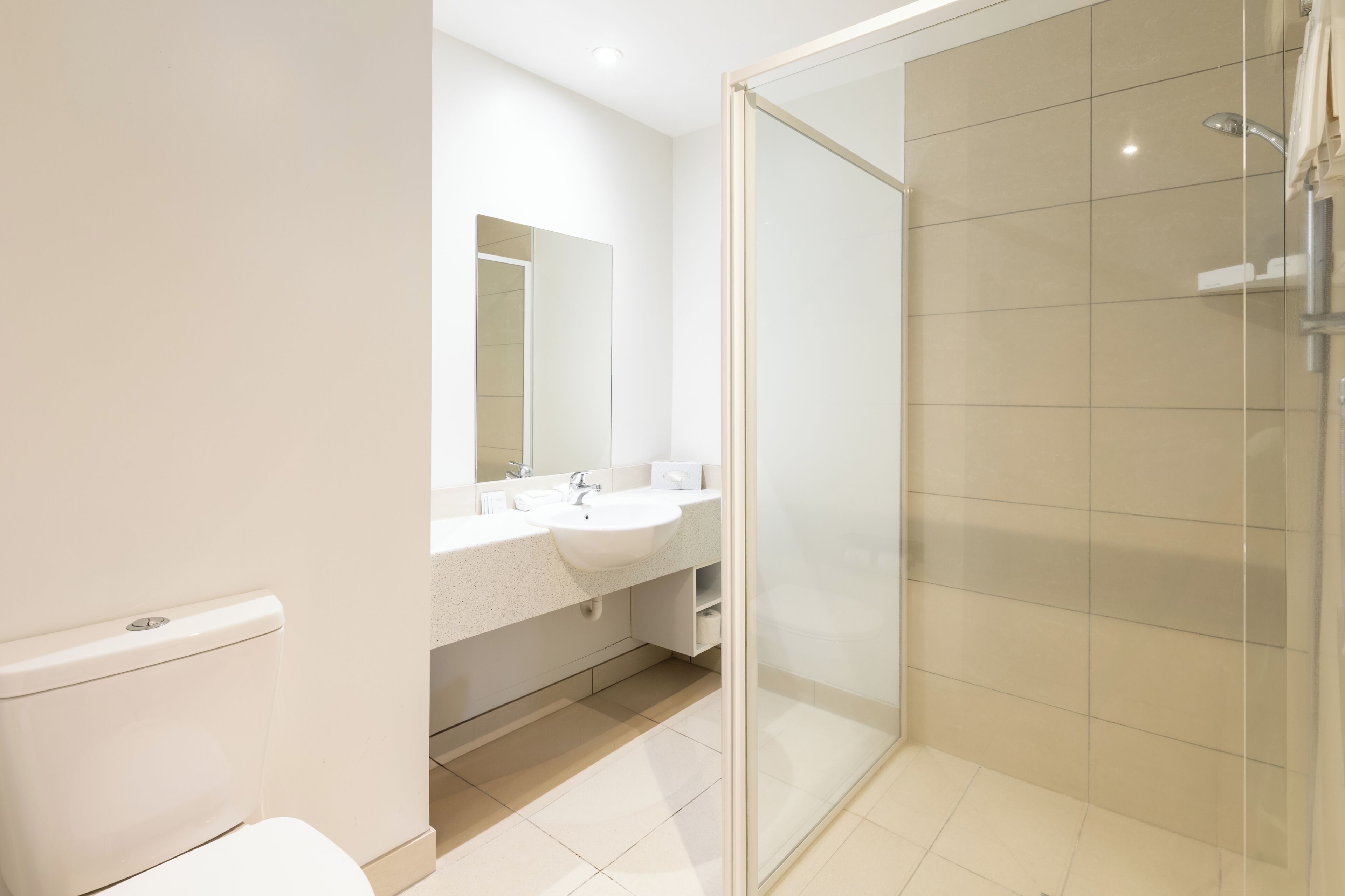 A modern bathroom with a toilet, sink, mirror, and glass shower enclosure.