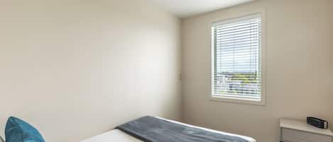 Een slaapkamer met een bed, een nachtkastje, een raam met jaloezieën en uitzicht op buiten.
