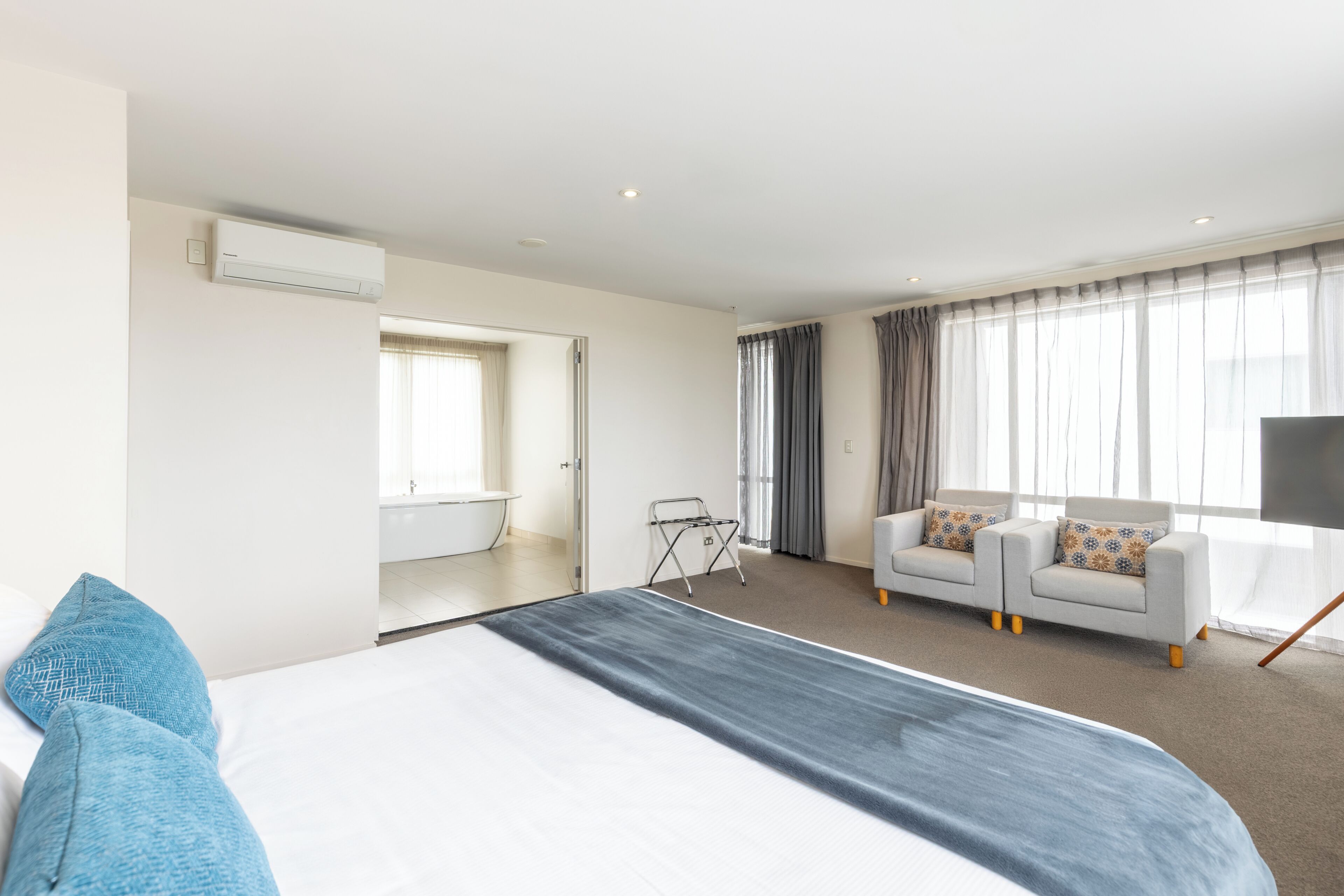 Une chambre d’hôtel moderne avec un grand lit, un canapé, une télévision et une vue sur la salle de bain.