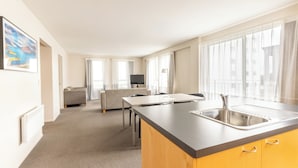Een moderne hotelkamer met kitchenette, een bank, een televisie en grote ramen.