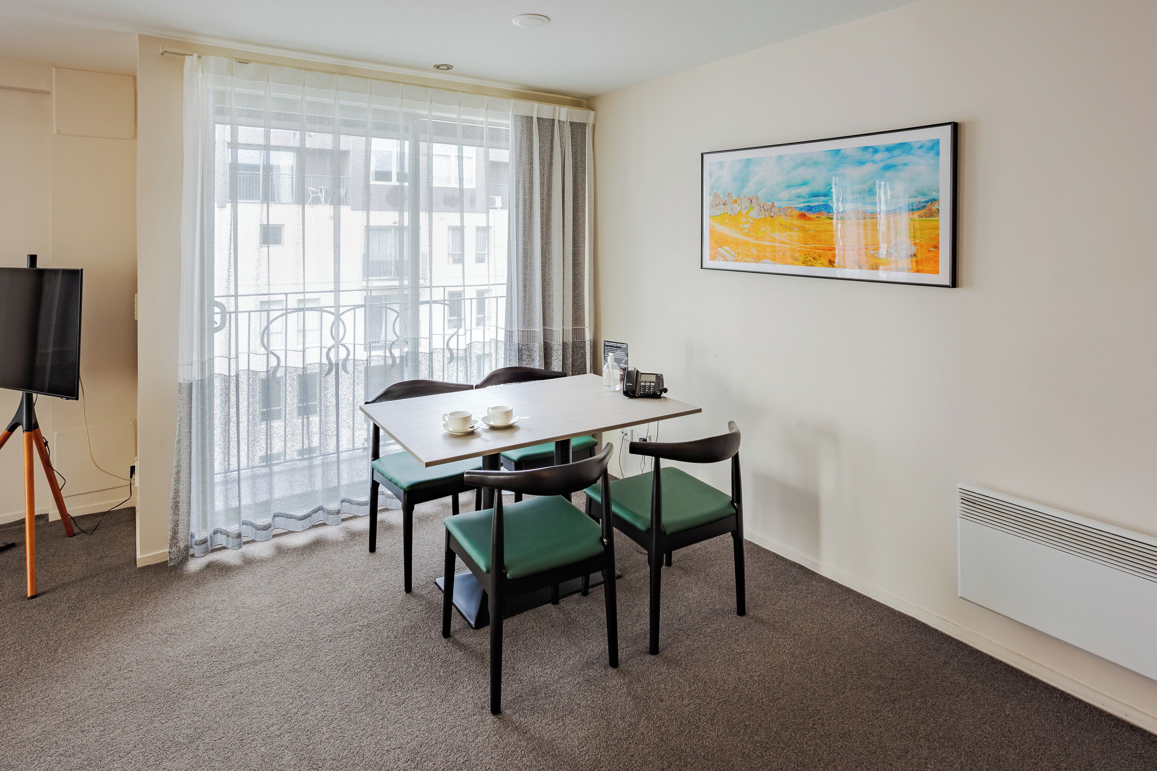 A hotel room with a balcony, a dining table with chairs, a flat-screen TV, and a painting on the wall.