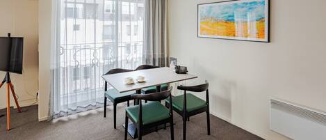 A hotel room with a balcony, a dining table with chairs, a flat-screen TV, and a painting on the wall.