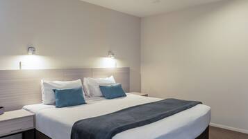 A hotel room with a bed, bedside tables, and wall-mounted lighting.