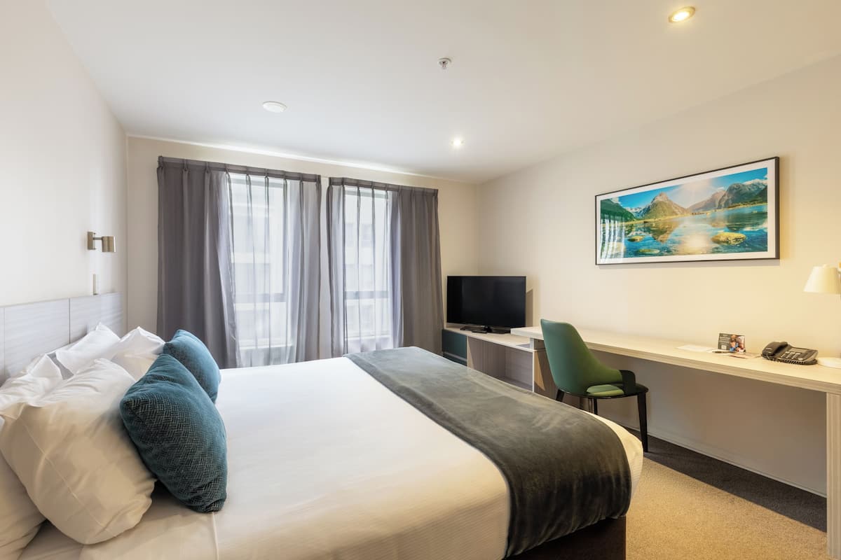 Een hotelkamer met een bed, een bureau, een stoel, een televisie en een schilderij aan de muur.