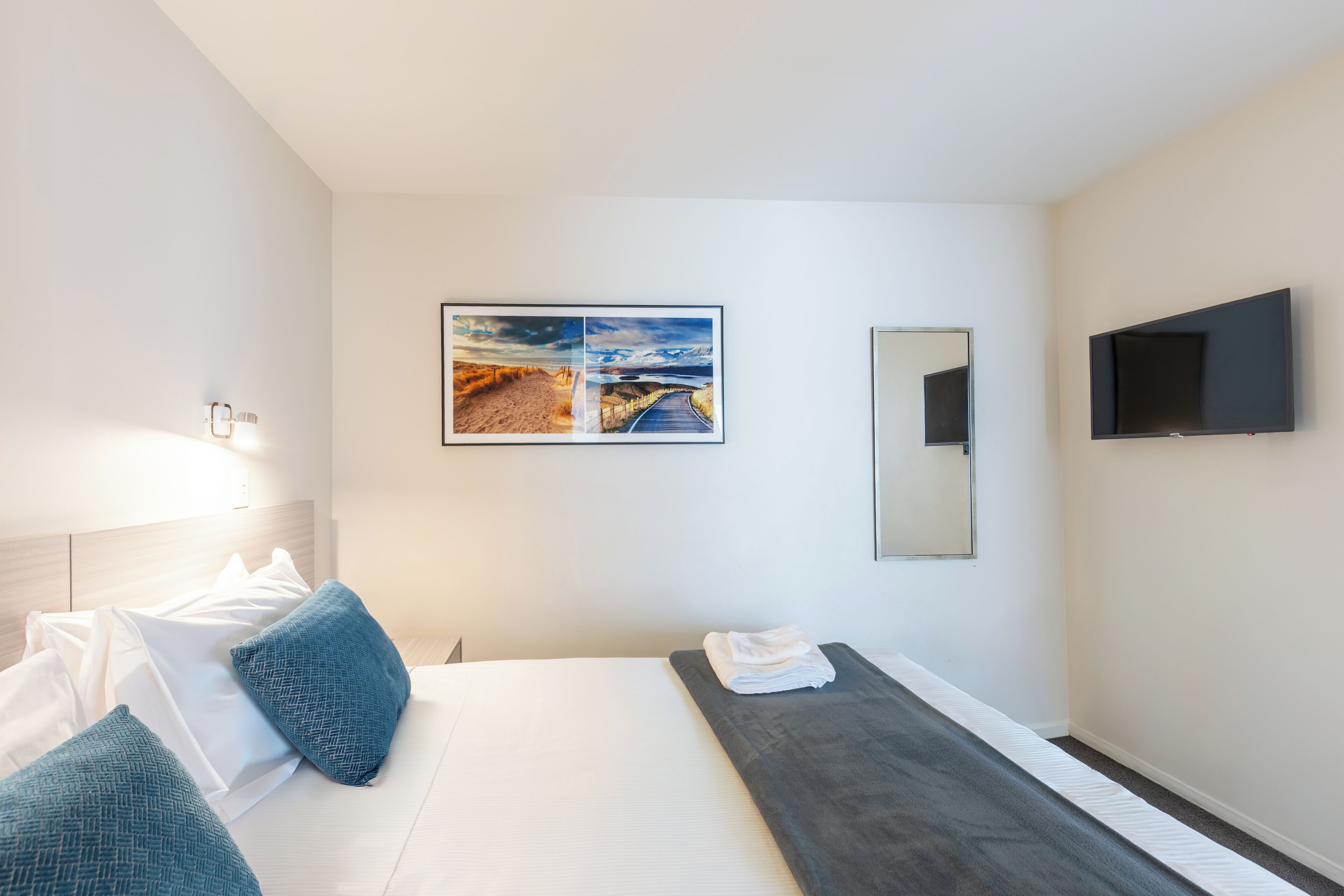 A hotel room with a bed, a flat-screen TV, a painting, and a mirror.
