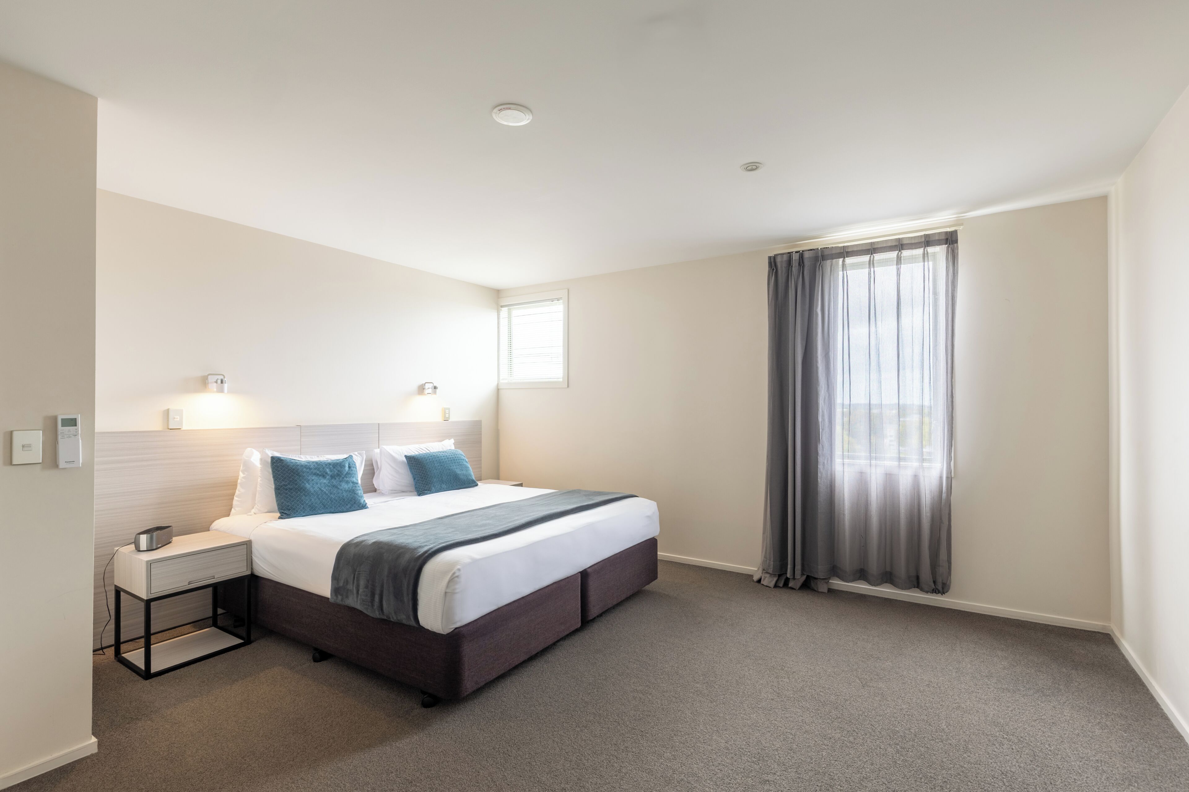Une chambre d’hôtel avec un lit, une table de chevet, une lampe et une fenêtre avec des rideaux.