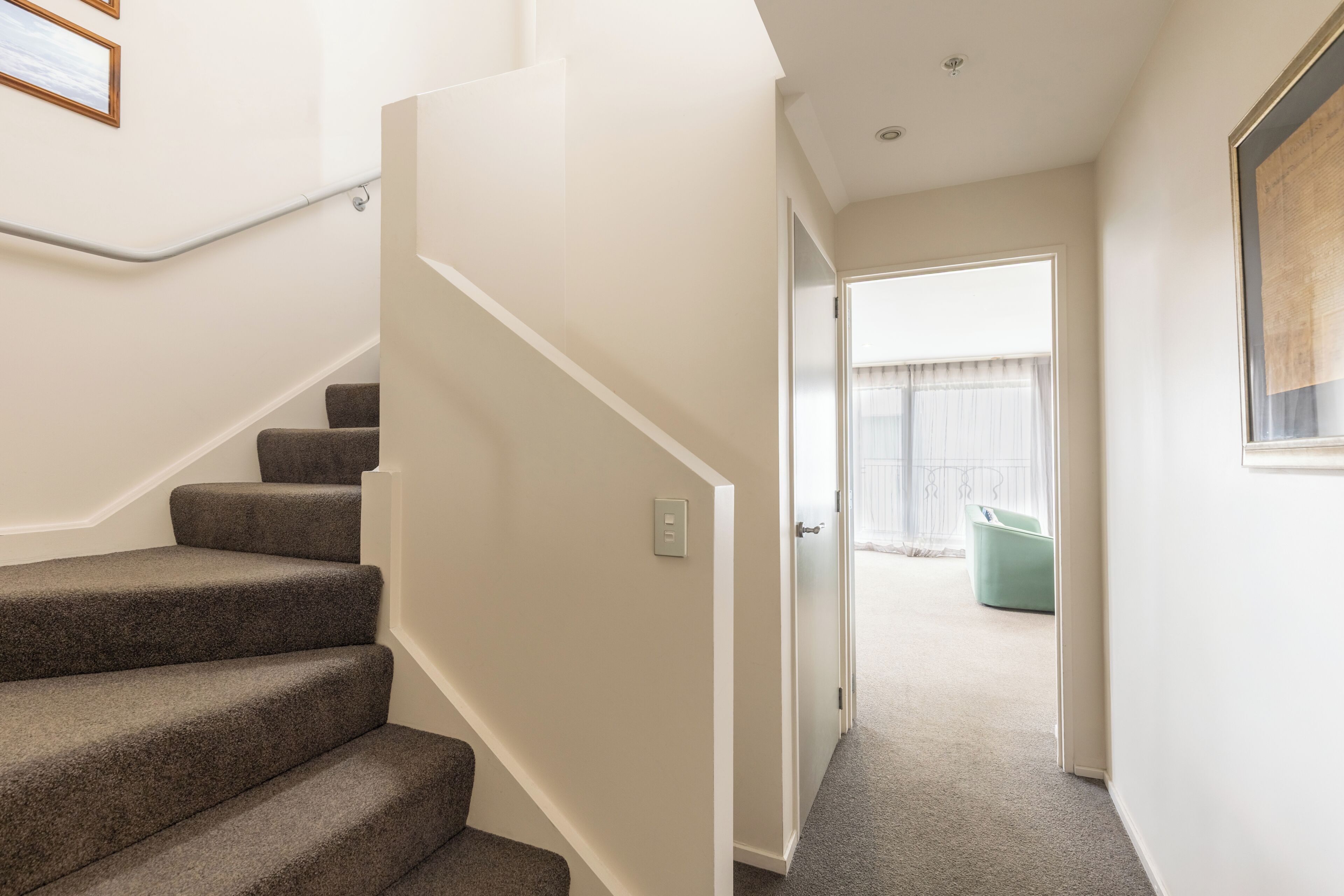 A staircase leading to a room with a door, a light switch, and a framed picture on the wall.
