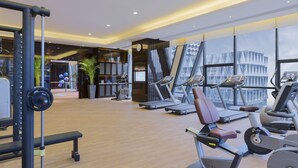 Une salle de sport moderne équipée de machines de cardio, d’appareils de musculation et dotée d’une grande fenêtre offrant une vue sur le paysage urbain.