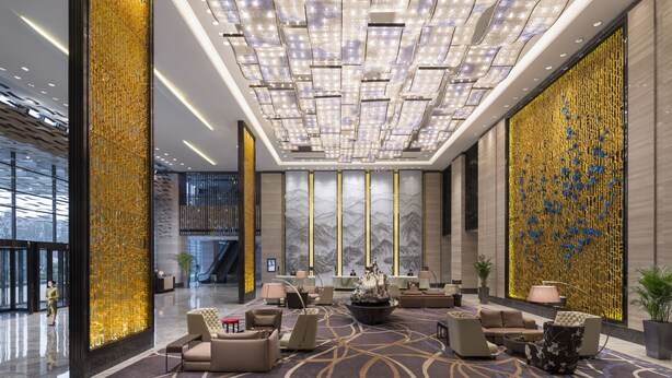 Un hall d’entrée spacieux agrémenté d’un lustre moderne, d’un coin salon et d’un grand mur décoratif.
