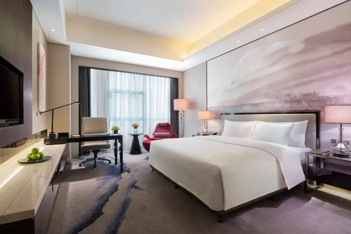 Une chambre d’hôtel avec un grand lit, un bureau avec une chaise, une télévision et une fenêtre avec des rideaux.
