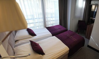 Habitación de hotel con dos camas, cada una con una colcha blanca y morada, una mesita de noche y una silla.