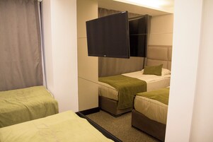 Habitación de hotel con dos camas individuales, un televisor de pantalla plana y una pequeña zona de estar.
