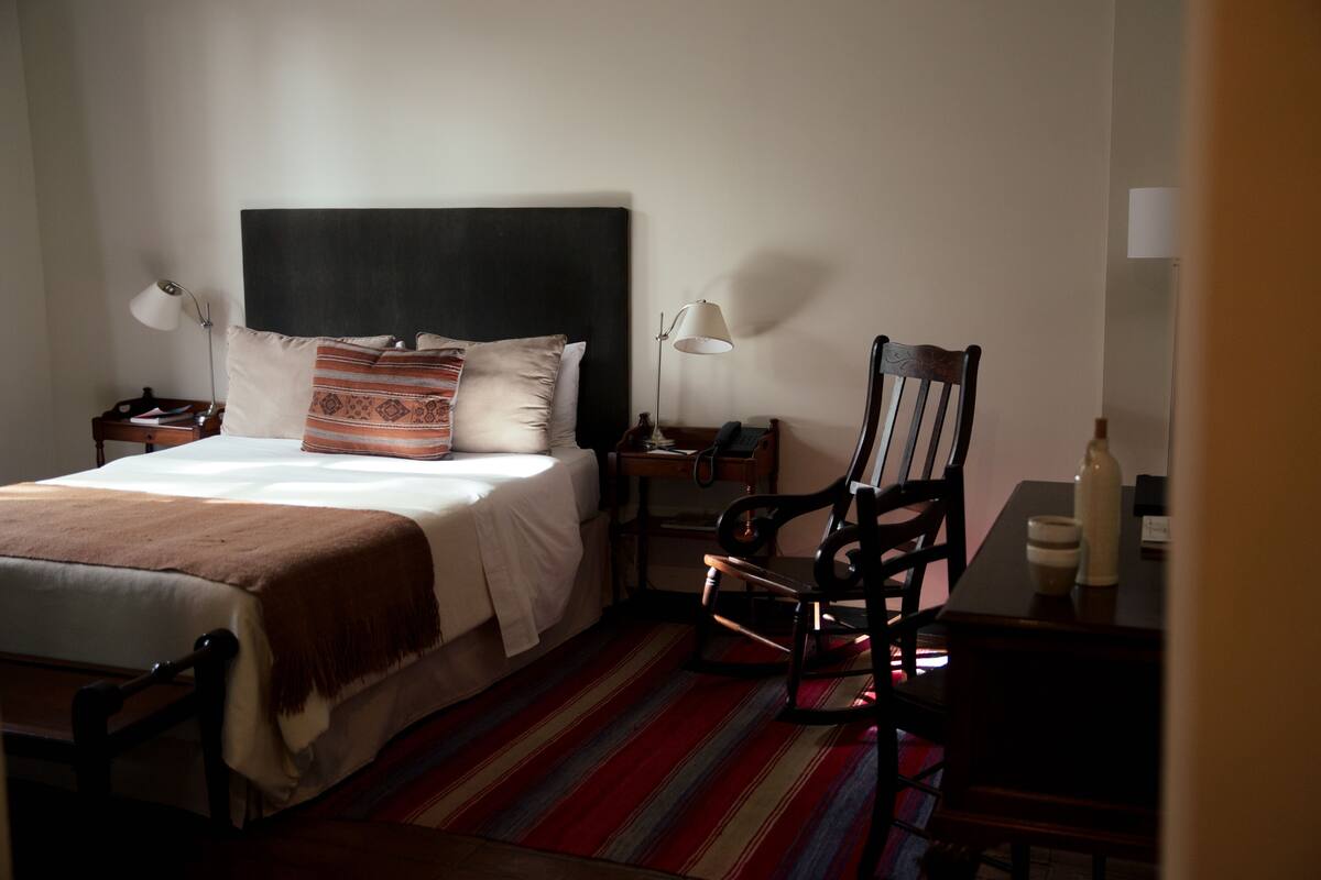 Habitació d'hotel amb un llit, taules de nit, una cadira, escriptori i una làmpada.