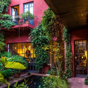 A red building with a balcony, a small garden area with plants, and a pool. - Be Jardin Escondido by Coppola (Buenos Aires)