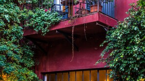 Un bâtiment rouge doté d’un balcon, entouré d’une végétation luxuriante et muni d’une grande fenêtre.