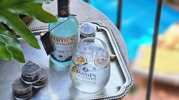 Un balcón con una bandeja metálica que sostiene una botella de ginebra J.E. Jardín Escondido, un vaso con hielo y rodajas de cítricos deshidratados, y pequeños recipientes con especias.