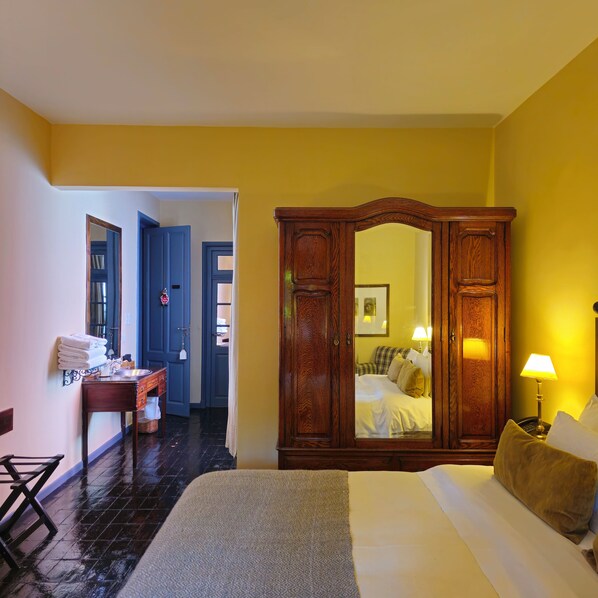 Habitación de hotel con cama, armario de madera, escritorio con silla y baño visible a través de una puerta abierta.