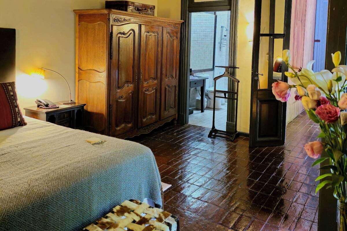 Una habitació amb un llit, un armari de fusta, una cadira, escriptori i una porta que dóna a l'exterior.