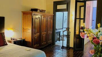 Una habitación con cama, armario de madera, una banca, escritorio y puerta que da al exterior.