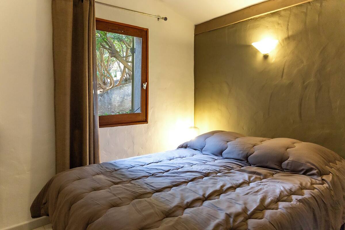 A bedroom with a bed, a window, and a wall-mounted light fixture.