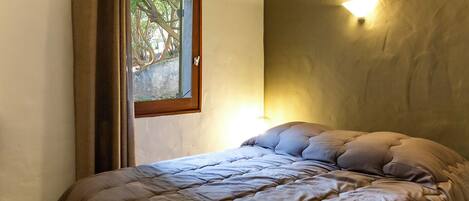 A bedroom with a bed, a window, and a wall-mounted light fixture.