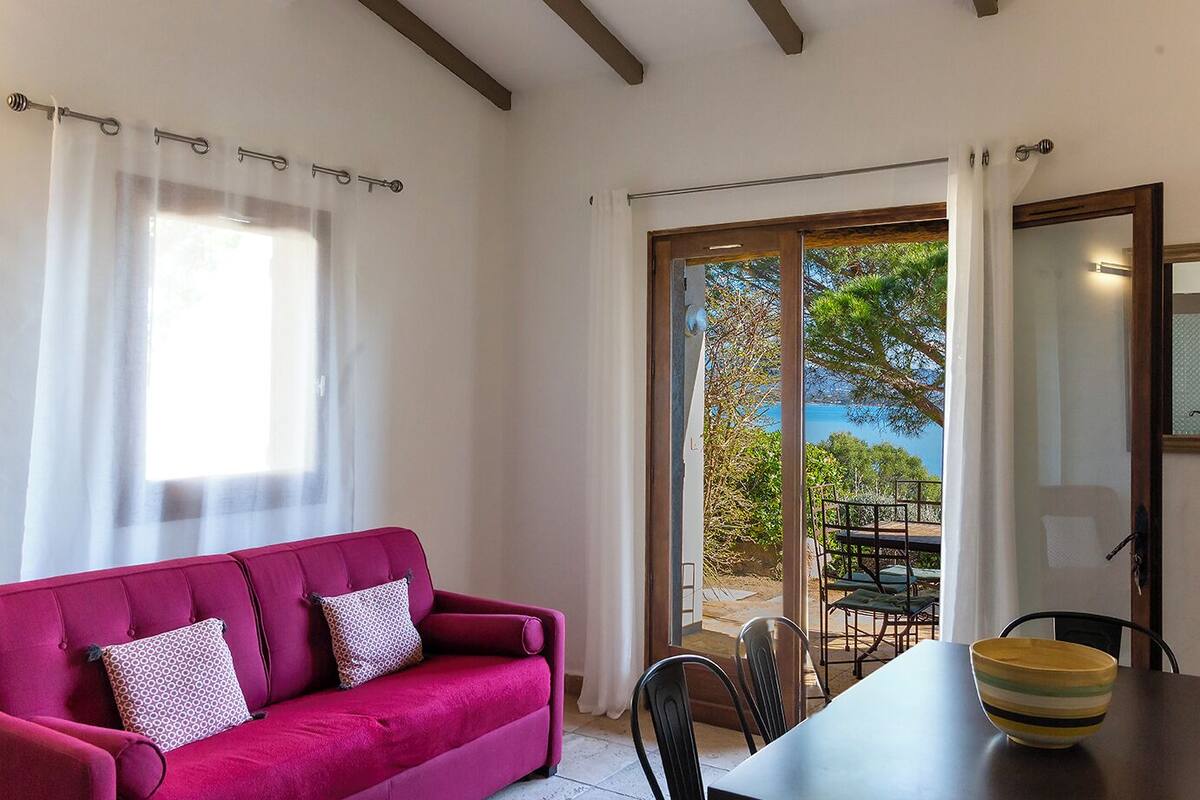 A room with a red sofa, a dining table with chairs, and a view of the outdoors through a glass door.