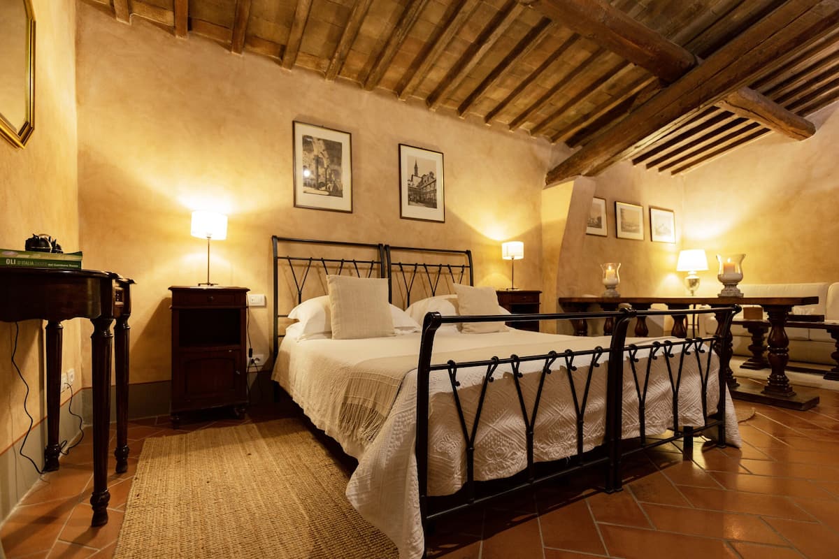 Een slaapkamer met een hemelbed, houten plafond en ingelijste foto’s aan de muur.