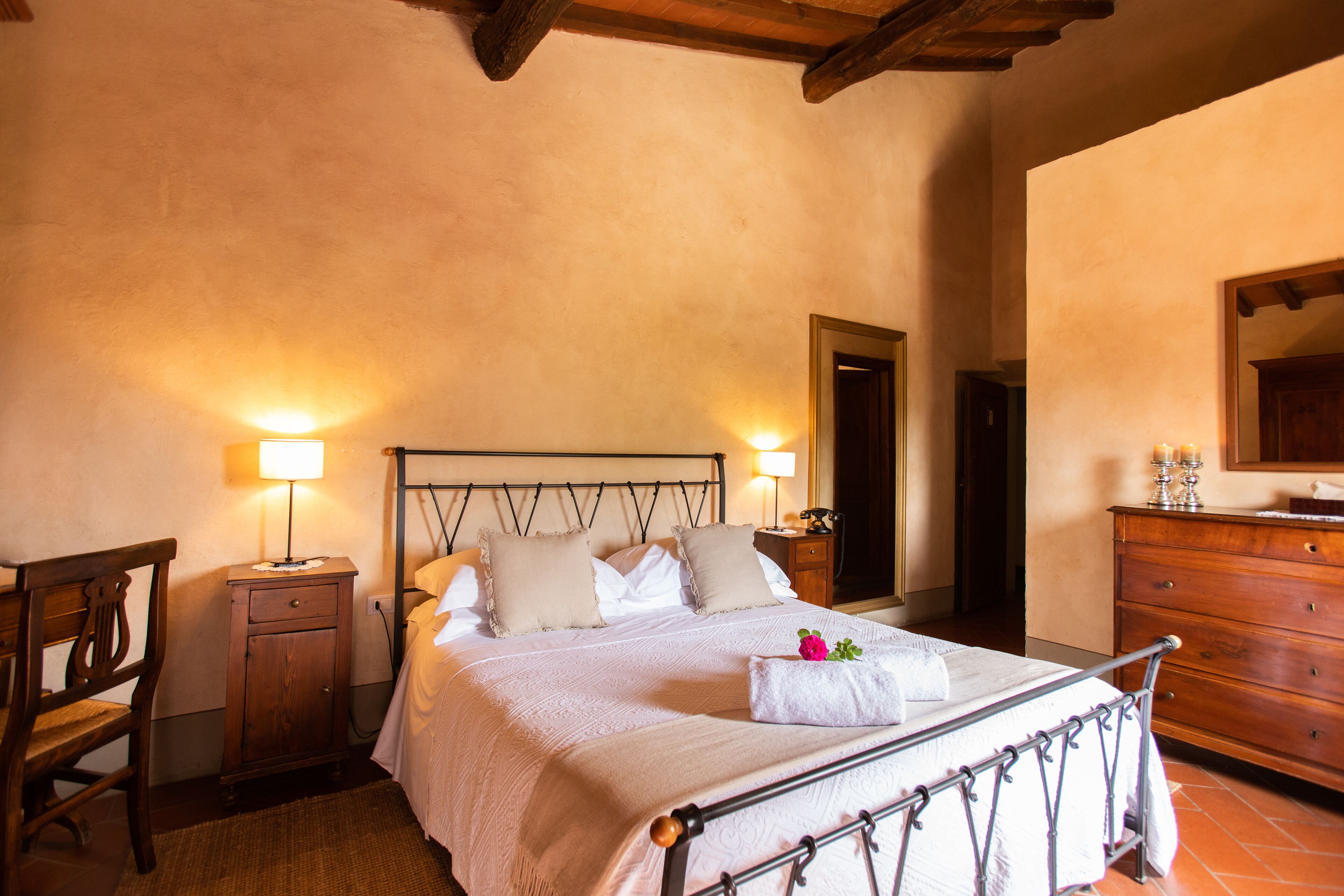 A neatly made bed with a headboard, bedside tables with lamps, a wooden dresser, and a mirror on the wall.