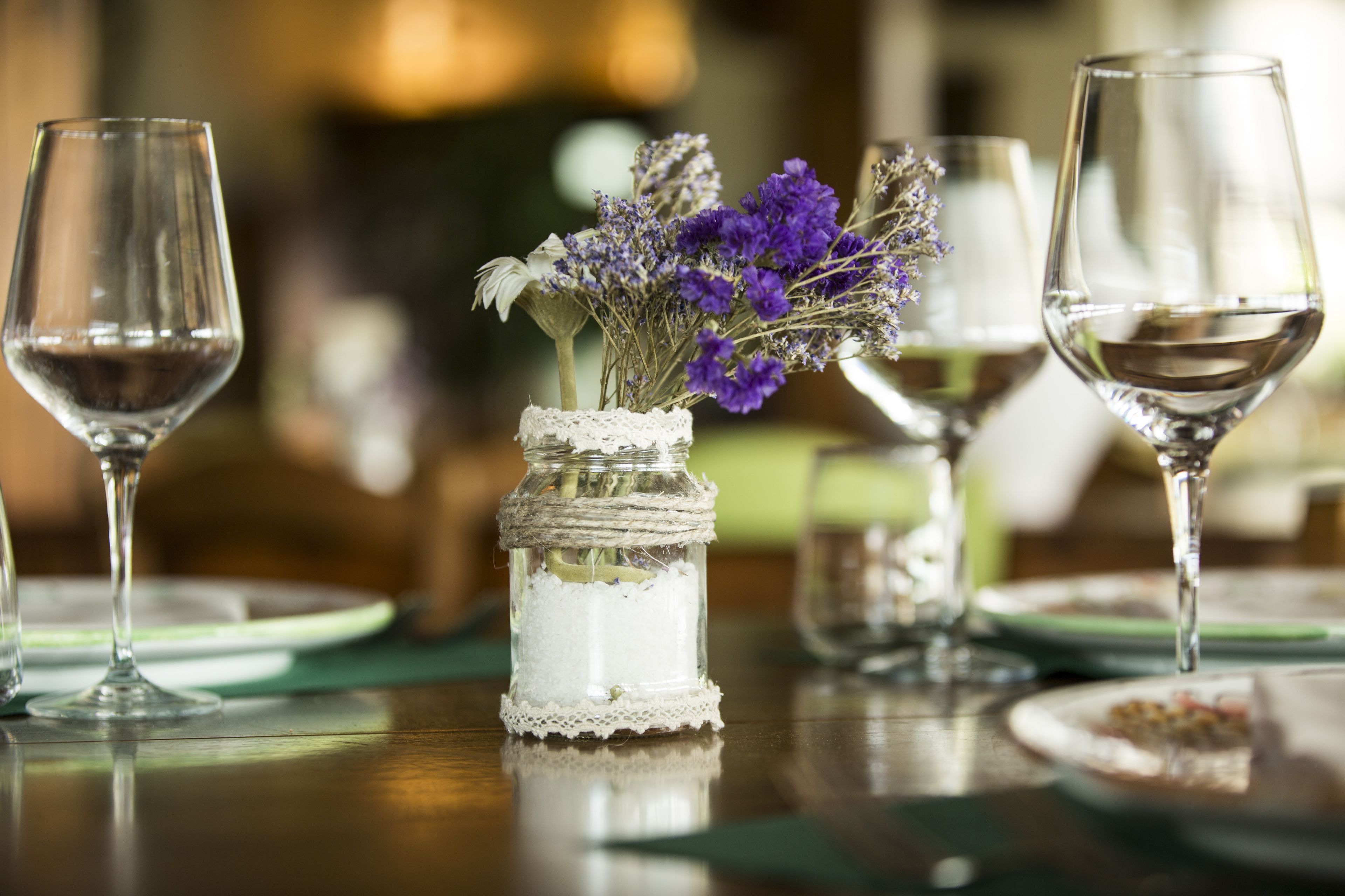 A table set with wine glasses, plates, and a small vase with dried flowers.