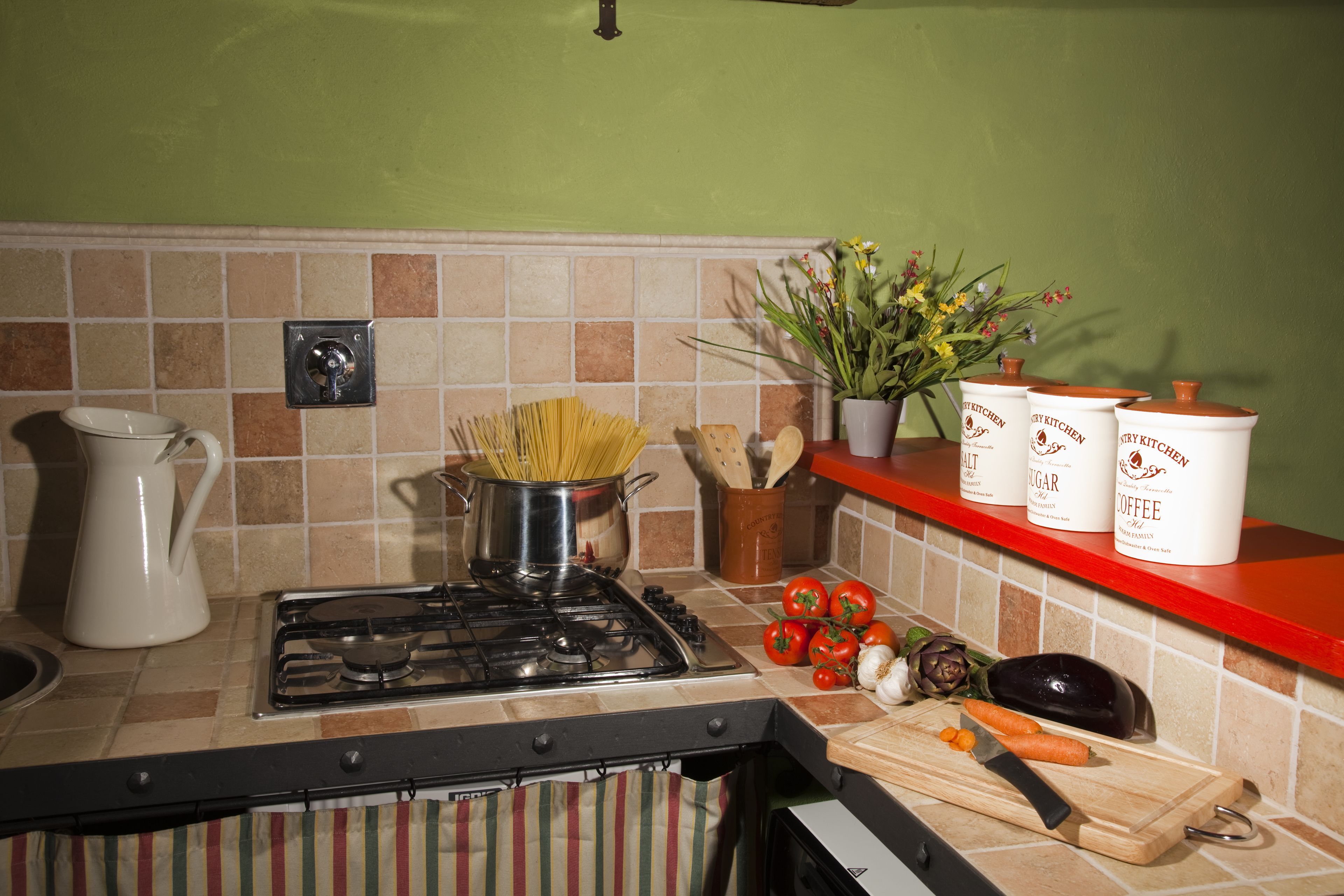 Una cocina con estufa, ollas, una tabla de cortar con verduras y un estante con recipientes.