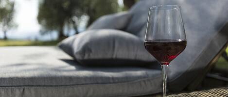 A glass of red wine on a wicker table with grey cushions in the background.