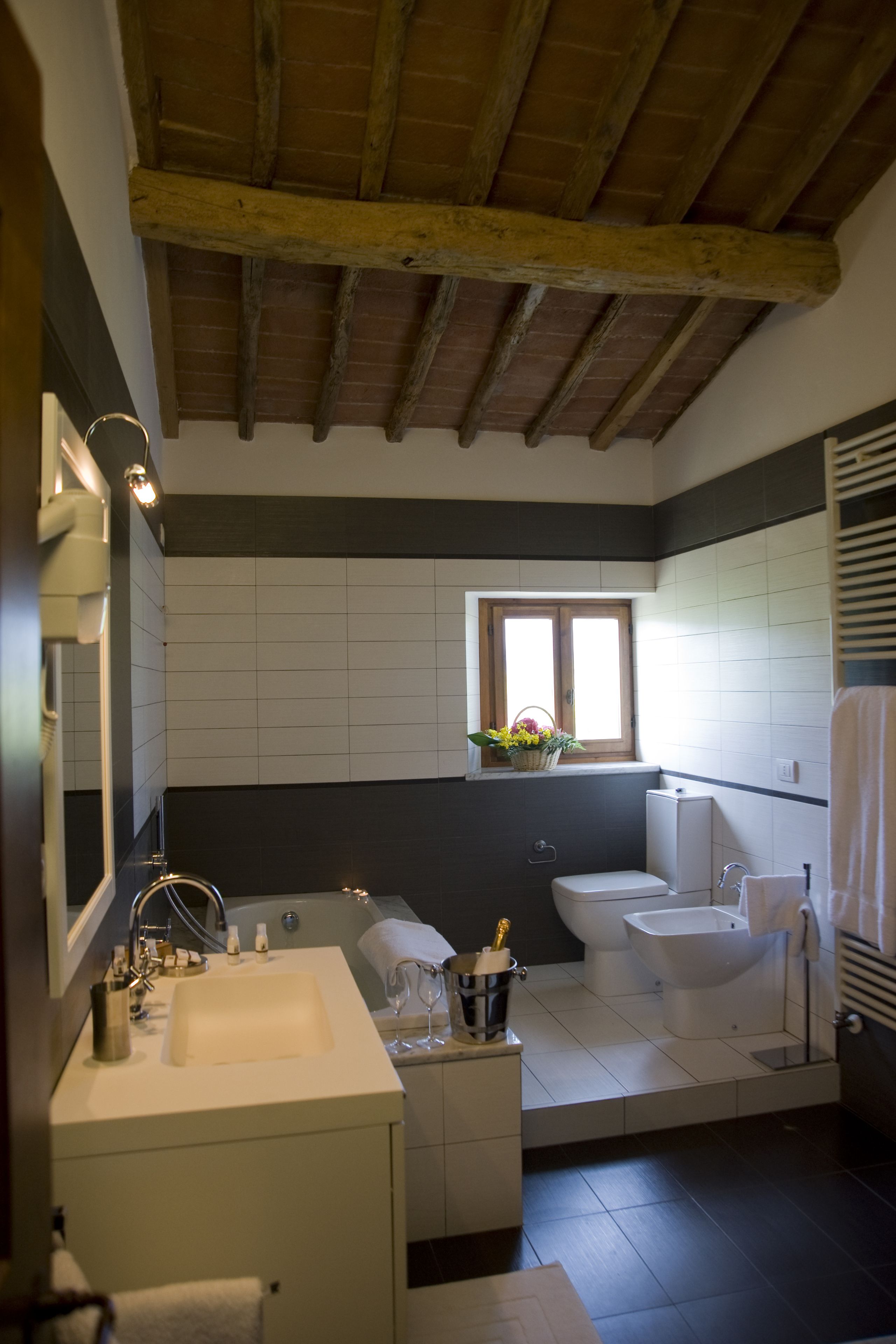 A bathroom with a wooden ceiling, a window with a basket of flowers, a bathtub, a sink, and a toilet.