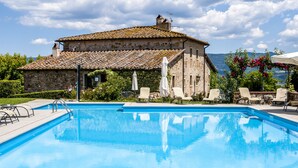 Une piscine avec des chaises longues et, en arrière-plan, un bâtiment en pierre.