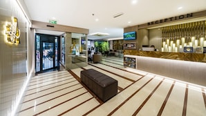 A hotel reception area with a reception desk, a television, and a seating area with a brown ottoman. - Aprilis Hotel - Special class (Istanbul)