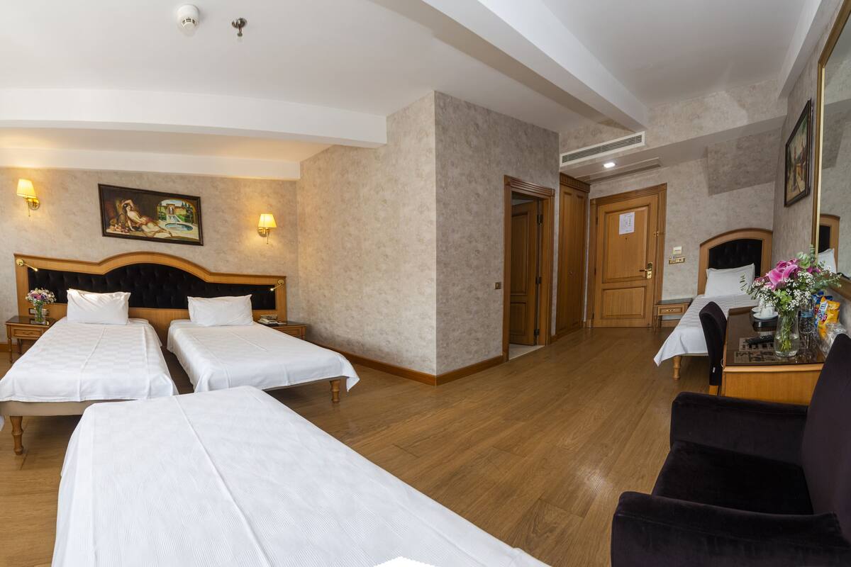 A hotel room with two single beds, a desk with a chair, a mirror, and a painting on the wall.