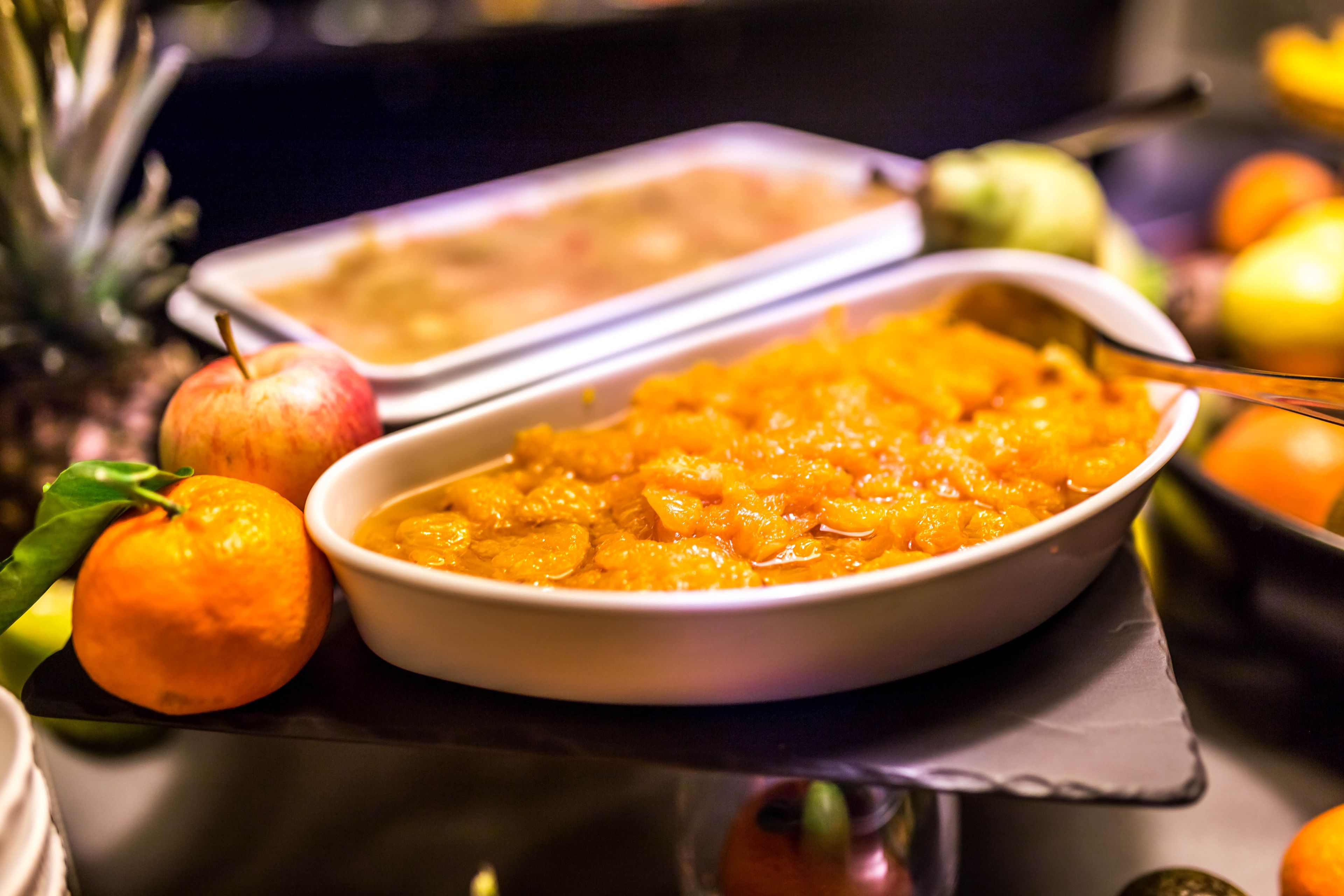 A buffet table with various dishes, including a bowl of orange-colored food and a tray of food in the background.