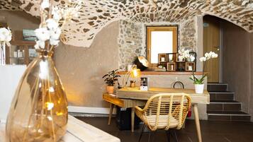 A rustic interior with a stone ceiling, a wooden table, wicker chairs, and potted plants.