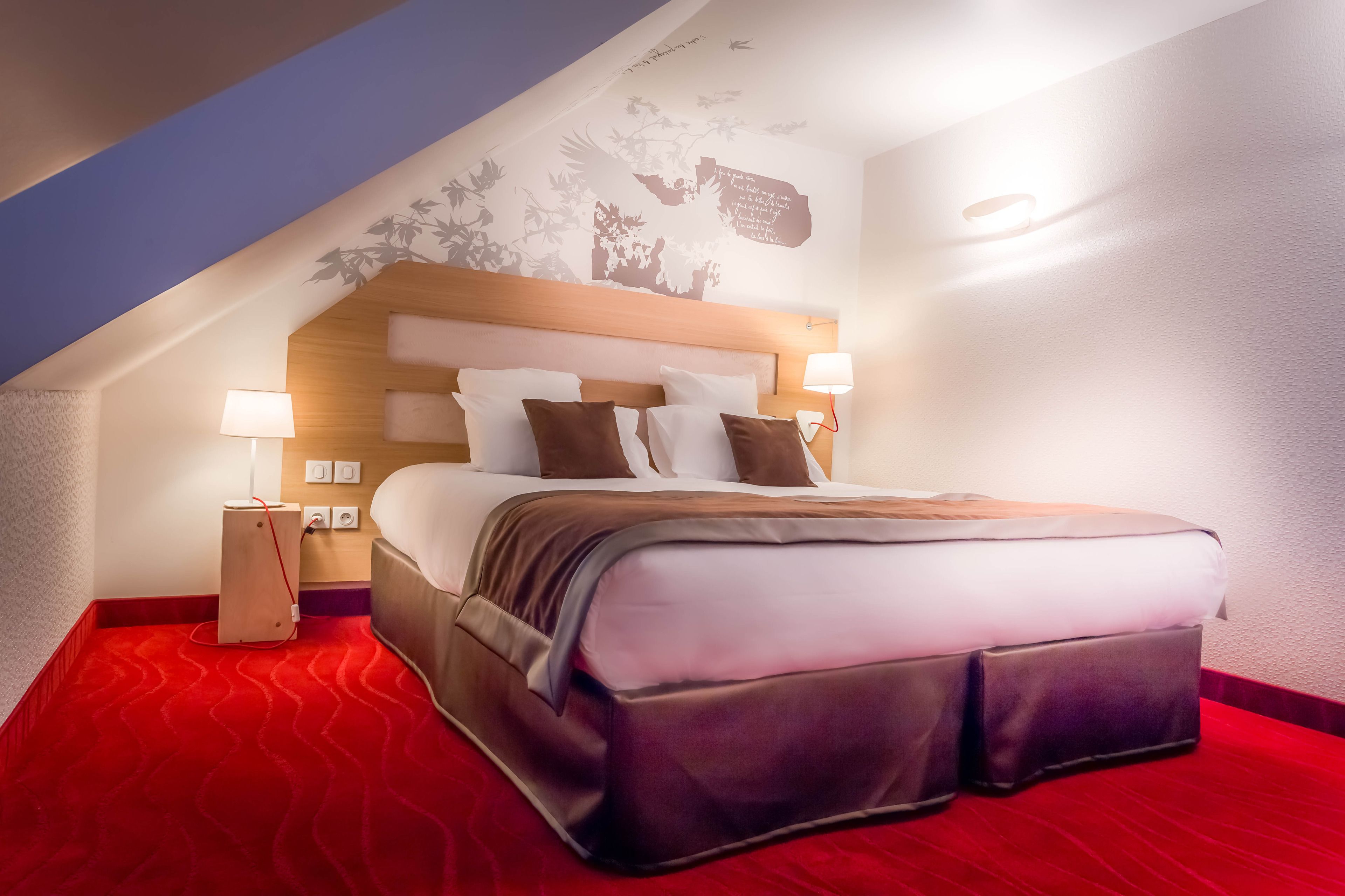 A hotel room with a large bed, a wooden headboard, two bedside lamps, a red carpet, and a wall mural.
