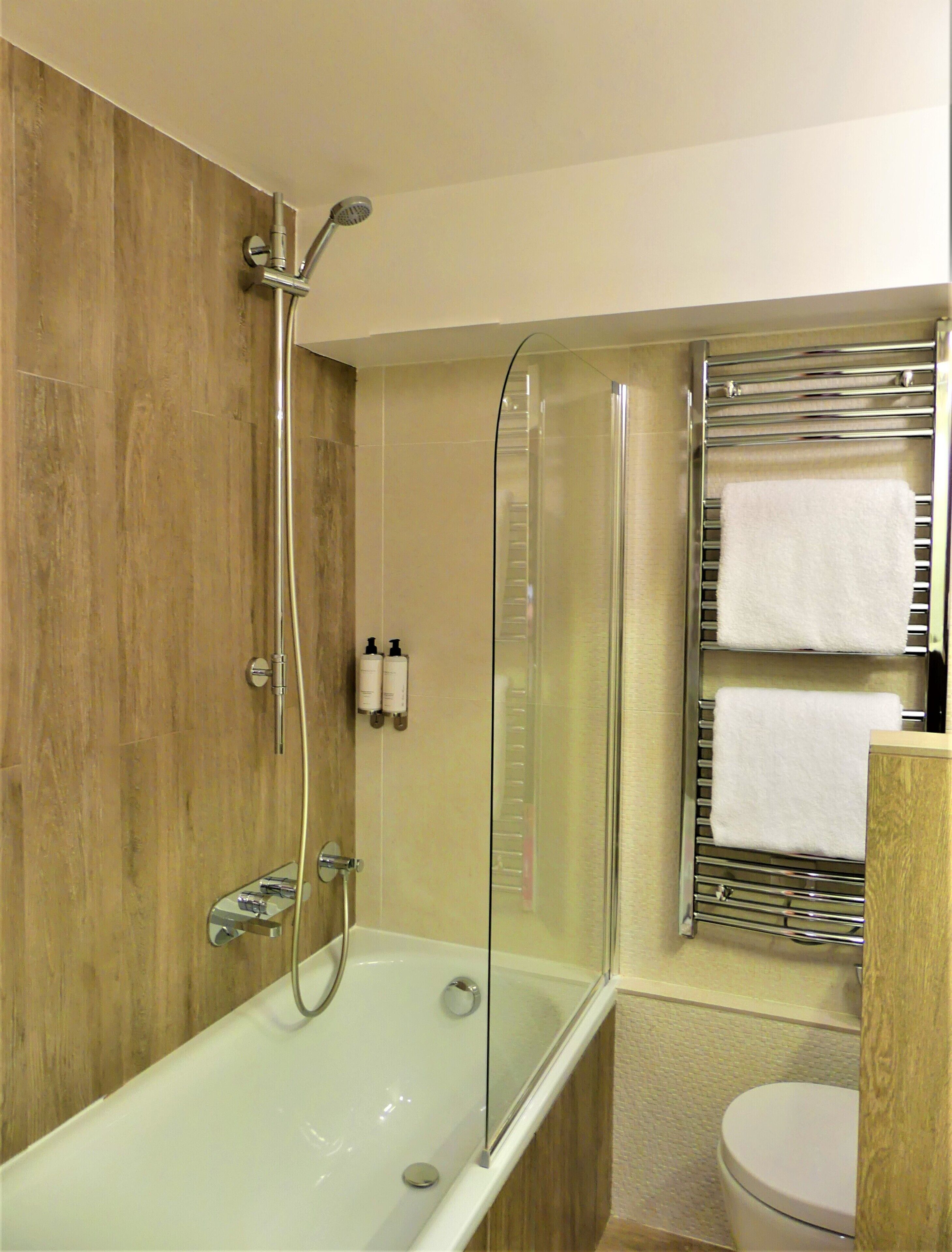 A modern bathroom with a glass-enclosed shower, a white bathtub, and a toilet.