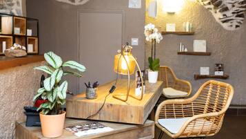 Un comptoir d’accueil en bois, une lampe, une plante en pot et des chaises en osier.