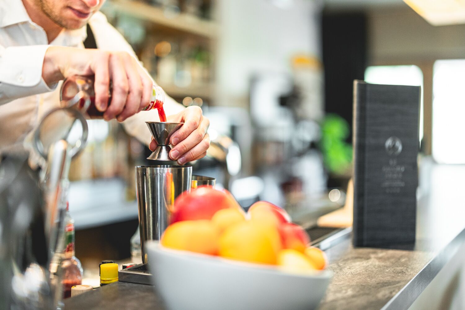 A bartender preparing a drink with a shaker and a bottle of sauce.